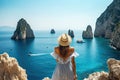 Young woman in white dress and hat standing on the cliff above the sea in Capri island, Italy, Holidays on Capri Island. Back view Royalty Free Stock Photo