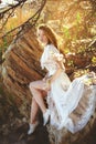 Young woman in white dress is sitting on the stone under the branches