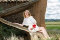 Young woman in white dress sitting on tree and holding poppies plants