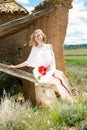 Young woman in white dress sitting on tree and holding poppies plants