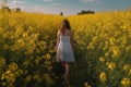 A young woman in a white dress walks through a field of yellow flowers. A young girl full rear view walks in a field of mustard