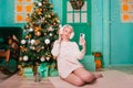 Young woman in white, fluffy headphones in Christmas decorations with a phone in her hands. a smartphone