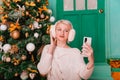 Young woman in white, fluffy headphones in Christmas decorations with a phone in her hands. a smartphone