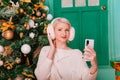 Young woman in white, fluffy headphones in Christmas decorations with a phone in her hands. a smartphone