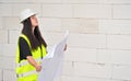 Young woman in white hard hat helmet and yellow green high visibility vest, standing next to construction wall, holding paper Royalty Free Stock Photo