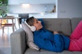 Young woman in white headphones enjoys listening to calm music and rests on comfortable sofa