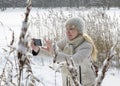 Young woman in a white jacket photographs winter canes of the forest lake coast on the phone