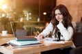 Young woman in white jacket working in her laptop taking notes in her planner looking annoyed while drinking hot coffee in cafe Royalty Free Stock Photo