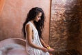 Woman in white lingerie relaxing near stone bath full foam in moroccan bathroom