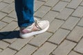 A young woman in white and pink sneakers and blue jeans is standing on the paved sidewalk. Summer walking, entertainment and Royalty Free Stock Photo