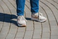 A young woman in white and pink sneakers and blue jeans is standing on the paved sidewalk. Summer walking, entertainment and Royalty Free Stock Photo