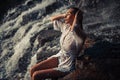 Young woman in white shirt and bikini sits on rock near waterfal Royalty Free Stock Photo