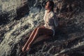 Young woman in white shirt and bikini sits on rock in water flow