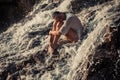 Young woman in white shirt and bikini sits on rock in water flow Royalty Free Stock Photo