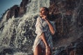 Young woman in white shirt and bikini stands near waterfall. Royalty Free Stock Photo