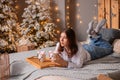 A young woman in a white shirt and blue jeans lies on a bed against a background of Christmas trees and bokeh of garlands Royalty Free Stock Photo