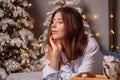 A young woman in a white shirt and blue jeans lies on a bed against a background of Christmas trees and bokeh of garlands Royalty Free Stock Photo