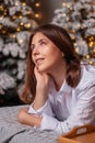 A young woman in a white shirt and blue jeans lies on a bed against a background of Christmas trees and bokeh of garlands Royalty Free Stock Photo