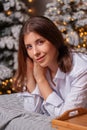 A young woman in a white shirt and blue jeans lies on a bed against a background of Christmas trees and bokeh of garlands Royalty Free Stock Photo