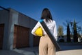 Young woman in white shirt, brown pants, with yellow workman`s helmet under her arm and blueprint tube hanging on her back.