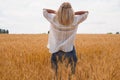 A young woman in a white shirt enjoys the moment among the golden wheat field against the blue sky. View from the back. Place for Royalty Free Stock Photo