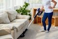 Young woman in white shirt and jeans cleaning carpet with vacuum cleaner in living room, copy space. Housework, cleanig and chores