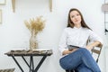 A young woman in a white shirt and jeans sits in a cafe at a table with a tablet in her hands. Female office worker at