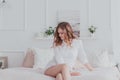 Young woman in white shirt sitting on bed and looking down Royalty Free Stock Photo