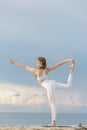 Young woman in white sportwear practicing yoga in the morning on seashore. Doing asana Natarajasana. Yoga at the beach Royalty Free Stock Photo