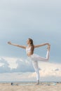 Young woman in white sportwear practicing yoga in the morning on seashore. Yoga at the beach. Doing asana Natarajasana Royalty Free Stock Photo