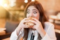 Young woman in white stylish blouse biting with appetite fresh tasty meat burger during lunch in trendy cafe looking very hungry Royalty Free Stock Photo