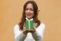 Young woman in white sweater with elf ears holding green gift box with bow in front of her. Christmas shopping concept. Royalty Free Stock Photo