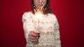 A young woman in a white sweater holds out a sparkler to the camera. Shooting in the studio on a red background. Royalty Free Stock Photo