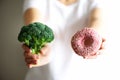 Young woman in white T-shirt choosing between broccoli or junk food, donut. Healthy clean detox eating concept