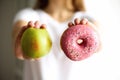 Young woman in white T-shirt choosing between green apple or junk food, donut. Healthy clean detox eating concept Royalty Free Stock Photo