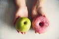 Young woman in white T-shirt choosing between green apple or junk food, donut. Healthy clean detox eating concept Royalty Free Stock Photo