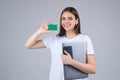 Young woman in white t-shirt holding credit card near face and laptop, isolated over gray background. Pay wit credit or Royalty Free Stock Photo