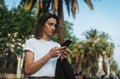 Young woman in a white t-shirt holding a smartphone after office work, hipster girl resting in a Park outside writing a message