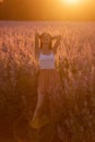 Young woman in white T-shirt, powdery shorts stands by blooming pink sage field. Portrait girls in the orange rays of the sun hair