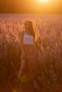 Young woman in white T-shirt, powdery shorts stands by blooming pink sage field. Portrait girls in the orange rays of the sun hair
