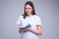 Young woman in white t-shirt writing with pen on notepad, isolated gray background. Student with notepad notebook Royalty Free Stock Photo