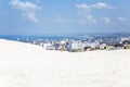 A young woman in a white tank top and denim shorts stands against the backdrop of a resort town on the sea on a sunny day. Royalty Free Stock Photo