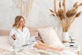 Young woman in white terry robe is drinking coffee and reading magazine or book in bedroom. Royalty Free Stock Photo