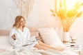 Young woman in white terry robe is drinking coffee and reading magazine or book in bedroom. Royalty Free Stock Photo