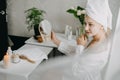 Young woman in white towel chilling in bedroom and making clay facial mask near mirror. Girl doing beauty treatment and Royalty Free Stock Photo