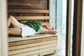 Young woman in white towel lies on wooden shelf in Finnish sauna Russian bath with rowan broom in spa hotel in front of the Royalty Free Stock Photo