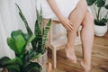 Young woman in white towel sitting in bathroom with green plants. Legs soft skin after shaving. Skin care and wellness concept Royalty Free Stock Photo