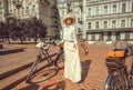 Young woman in white vintage dress standing with old bicycle before the start of festival Retro Cruise