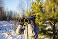 Young woman in winter clothes looking through binoculars in winter snowy pine forest. Birdwatching Royalty Free Stock Photo