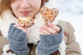 Young woman in winter coat and knitted grey mittens hold beautiful heart shaped biscuit cookies, one bitten, with white icing Royalty Free Stock Photo